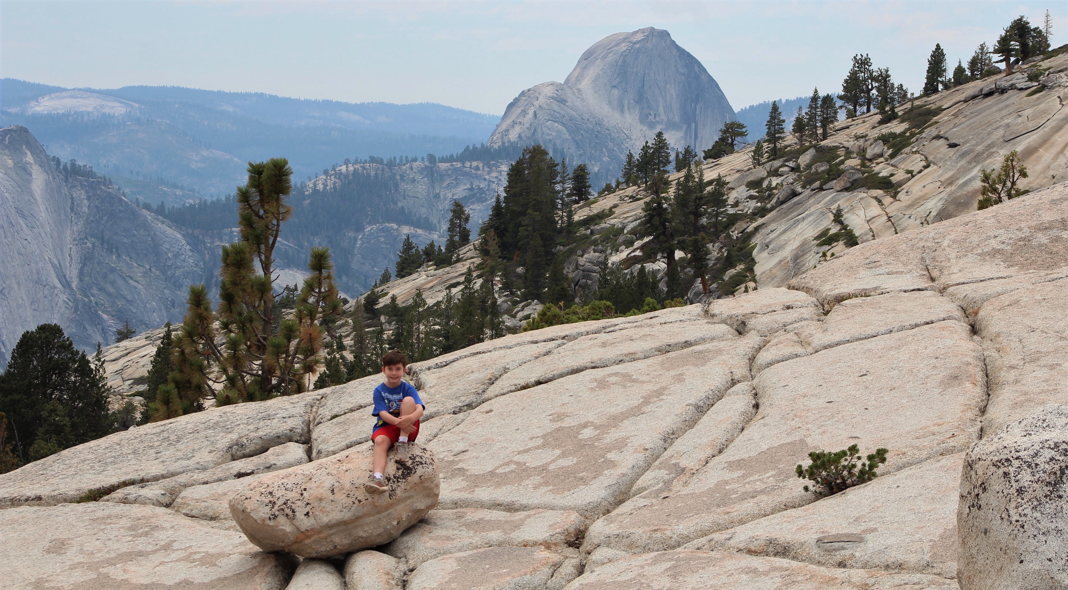 young boy sits on a large granite rock in Yosemite National Park